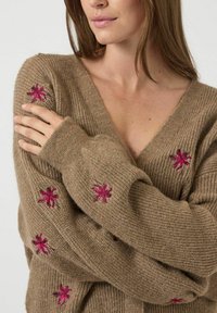 Maglione beige lavorato a maglia con scollo a V profondo, caratterizzato da ricami floreali rosa sulle maniche. Texture morbida con vestibilità comoda e maniche lunghe.