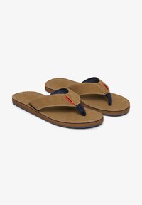 Chanclas marrones con una parte superior de ante suave, separador de dedo azul marino y detalles cosidos en una planta color beige. Suela de goma flexible.