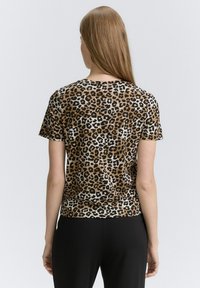 Majica s leopard uzorkom od mekog materijala, s kratkim rukavima i okruglim izrezom. Boje uključuju svijetlosmeđu, smeđu i crnu.