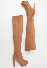 Brązowe kozaki z sztucznego zamszu, sięgające za kolano, z wysokim obcasem, bocznym zamkiem błyskawicznym i gładką teksturą. Posiadają platformę i prosty krój.