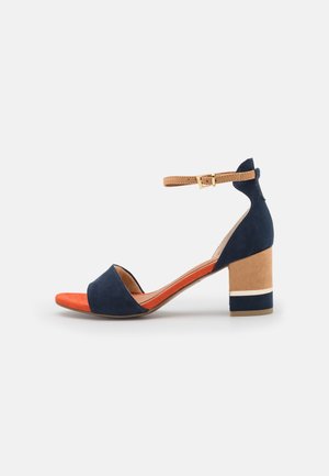 Sandale à talon bloc pour femme avec bout ouvert, brides bleu marine, bride de cheville beige avec boucle et semelle intérieure orange, présentée sur fond blanc.