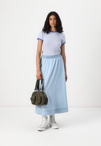 Gonna maxi in denim azzurro, blusa a righe a maniche corte con dettagli blu, sneakers bianche e borsa verde oliva con tasche.