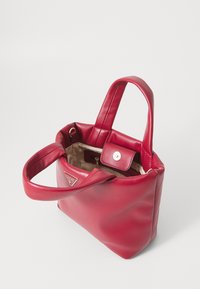 Borsa tote in pelle rossa con una texture morbida, dotata di due manici, chiusura a pressione e una tasca interna. Dettaglio del logo sul davanti.