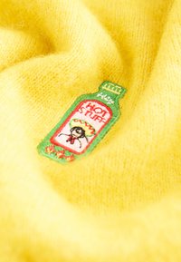 Patch brodé de bouteille de sauce piquante avec une personne portant un sombrero sur un fond de tissu jaune doux et duveteux.