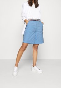 Jasnoniebieskie szorty o luźnym kroju, z płaskim przodem, bocznymi kieszeniami oraz paskiem w paski; stylizowane z białą koszulką i białymi trampkami.