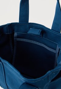 Μπλε τσάντα υφάσματος με διπλές λαβές, εμφανές εσωτερικό τσέπη και κλείσιμο με μαγνητικό κούμπωμα, εμφανιζόμενη ανοιχτή σε λευκό φόντο.