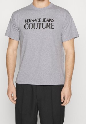 Grijze katoenen T-shirt met een zwarte "VERSACE JEANS COUTURE" opdruk aan de voorkant, ronde halslijn en korte mouwen.