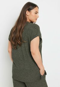 Vihreä neulepaita, jossa on lyhyet kapeat hihat, rento istuvuus ja ribbeerattu pinta. Takana on sivurei'ät ja taskut.