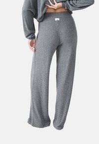 Person wearing ribbed, wide-leg gray knit pants and a matching gray sweater, hand resting on lower back, shown from behind.