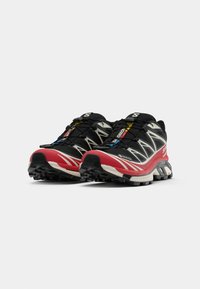 Schwarze und rote Laufschuhe mit einer strukturierten Sohle, die reflektierende Akzente und ein sicheres Schnürrsystem für eine anpassbare Passform bieten.