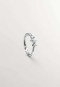 Anillo de joyería con una banda de plata pulida, tres piedras redondas transparentes dispuestas de manera asimétrica y un diseño suave y redondeado.