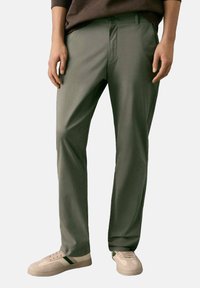 Pantaloni verdi leggeri con una texture liscia, design a gamba dritta e tasche frontali. Abbinati a sneakers beige.