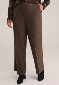 Bruine wijde broek met een zachte textuur en voorplooien, gecombineerd met zwarte enkellaarsjes. De stof lijkt lichtgewicht en op maat gemaakt.