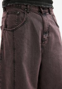 Pantaloni cargo in denim viola scuro con una vestibilità rilassata. Le caratteristiche includono ampi tasconi laterali, cuciture in vista e una vita sfilacciata.