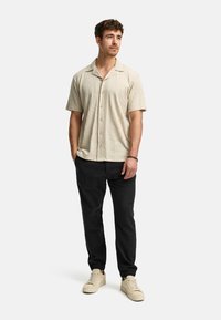 Lichtbeige shirt met korte mouwen met een gestructureerd verticaal patroon, gecombineerd met zwarte, taps toelopende broeken en beige sneakers.