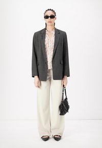 Grå rutete oversized blazer, blomstrete skjorte, kremfargede vide bukser, svart håndbagasje og spiss-tå sko. Tilbehør inkluderer solbriller.