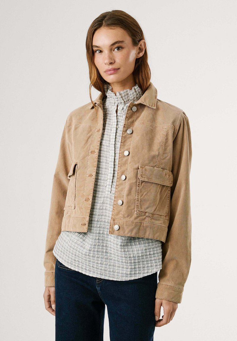 Beige corduroy jas met knopen aan de voorkant, twee zijzakken en een cropped ontwerp, gedragen over een geruit shirt.