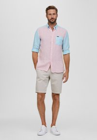 Leichtes, mehrfarbiges Hemd mit blauen und pinken Streifen, Brusttasche, kombiniert mit beigen Shorts und weißen Sneakers.