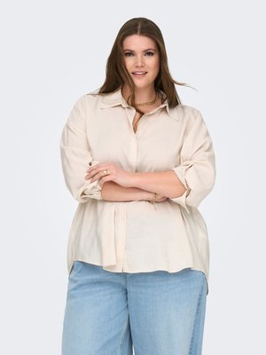 Light beige linen shirt with a collared neckline, button-up front, and rolled-up sleeves, paired with light blue loose-fit jeans.