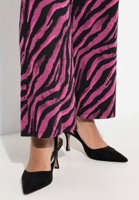Svarta mocka högklackade skor med spetsig tå och smal stilettklack, bärs tillsammans med rosa- och svarta zebra-mönstrade vida byxor.