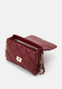 Sac à main en cuir bordeaux matelassé avec un fermoir en métal doré, une chaîne et un rabat ouvert révélant un intérieur doublé.