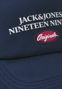 Gorra azul marino con texto blanco: "JACK&JONES NINETEEN NINETY" con un acento ovalado rojo que dice "Originals". Fabricada con tela texturizada.