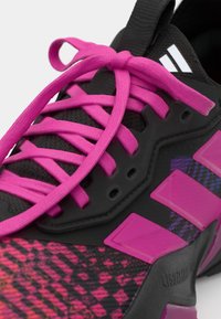 Svarte sportsko med rosa snører, teksturert mesh-overdel, mønstrete overlay i rosa og lilla, og signatur tre-stripe-logo på siden.