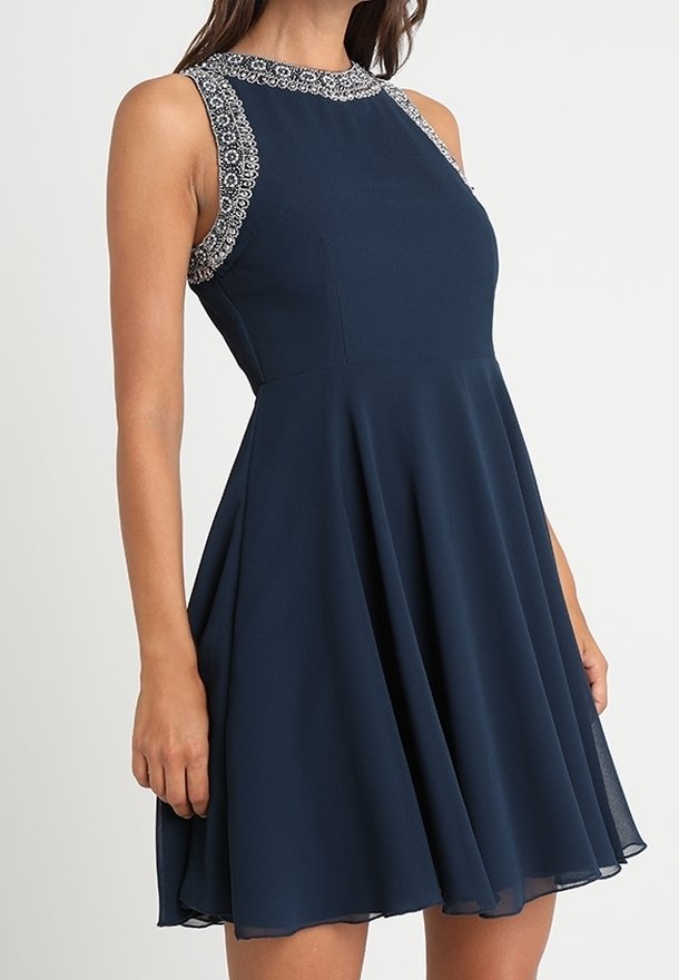 Robe sans manches bleu marine avec une jupe évasée et un délicat bord en dentelle blanche autour du décolleté et des emmanchures.