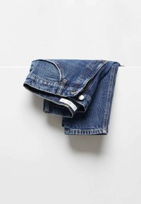 Jean en denim bleu plié et posé sur une surface horizontale blanche, sur un fond blanc uni.