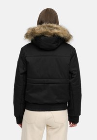 Black padded jacket with a removable beige fur-lined hood, ribbed cuffs, and a cropped design. Features visible stitching and a sleek back panel.