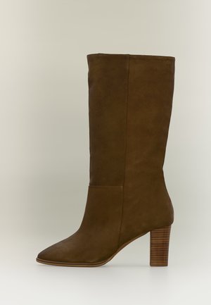 Bota de ante marrón hasta la mitad de la pantorrilla con tacón bloque apilado y punta puntiaguda, mostrada de perfil sobre un fondo neutro.
