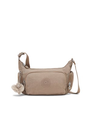 Kleine beige crossbodytas met voorvak met rits, ronde logopatch, zijvakjes en een pluche apensleutelhanger bevestigd aan de band.