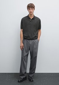 Polo shirt lavorato a maglia grigio scuro con colletto e tre bottoni, abbinato a pantaloni larghi grigio chiaro e scarpe in pelle nera.
