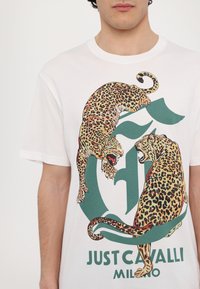 Biała bawełniana koszulka z dużą grafiką dwóch lampartów z żywymi plamkami, na zielonym tle z napisem "Just Cavalli Milano."