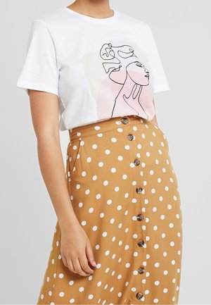 Biała koszulka z prostym rysunkiem twarzy, zestawiona z brązową spódnicą ozdobioną białymi kropkami i guzikami.