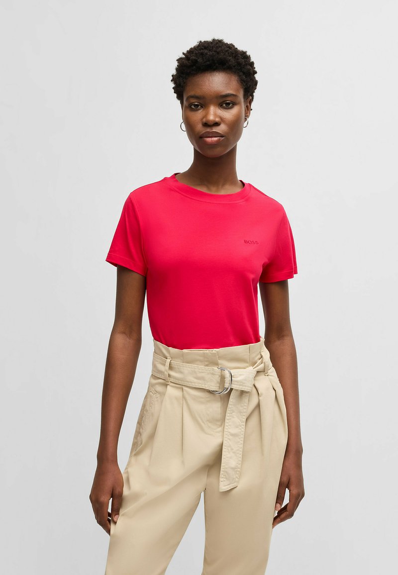 T-shirt rossa a maniche corte con collo rotondo e un logo del marchio discreto. Realizzata in un tessuto morbido, abbinata a pantaloni beige a vita alta con cintura.