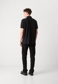 Zwarte poloshirt met een klassieke kraag, korte mouwen en een rechte zoom. Gekleed met zwarte broek en stevige zwarte schoenen.