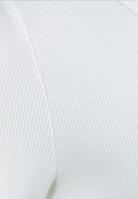 Weißer gerippter Stoff, der eine Nahaufnahme der Textur zeigt, mit einem leichten Glanz. Das Design weist einen sanften Übergang zwischen den Abschnitten auf.