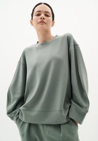 Př oversized mikina v tlumené zeleni, s kulatým výstřihem, spadlými rameny a měkkou, hladkou tkaninou s jemným pruhem.