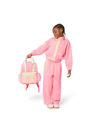 Ružová mikina a nohavice s elastickými manžetami, doplnené o viacvreckový batoh s priedušnou sieťovinou a farebnými akcentmi.