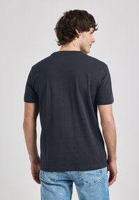 Tmavě šedé tričko s krátkým rukávem vyrobené z bavlny, s kulatým výstřihem a hladkou texturou. Nosené s světle modrými džíny.