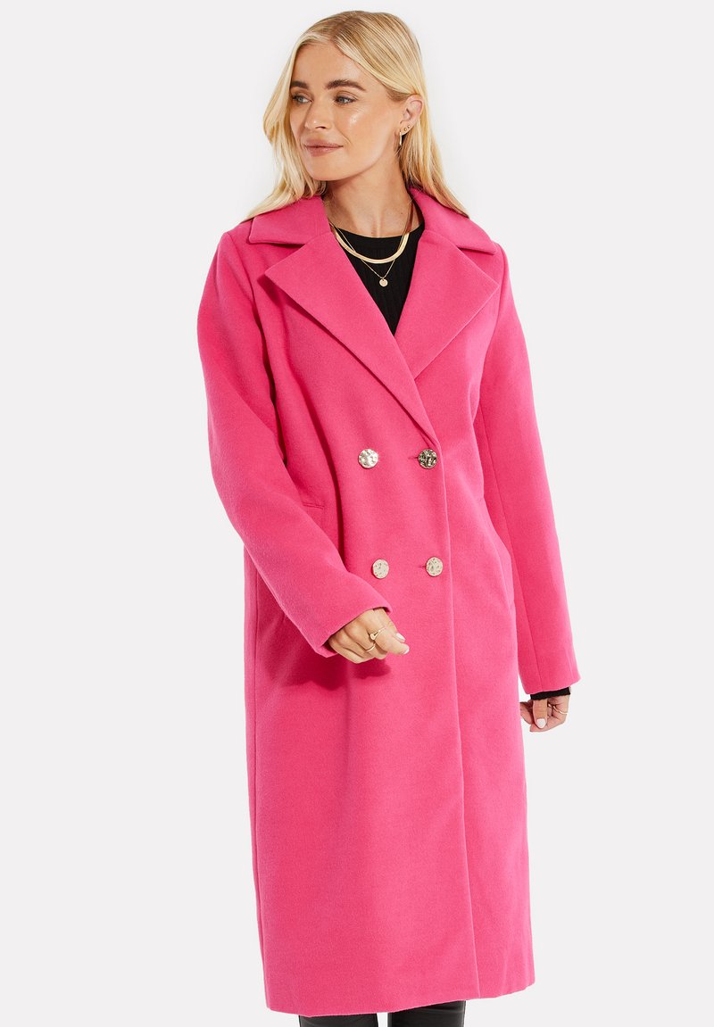 Cappotto rosa doppiopetto realizzato in morbido materiale, con collo a scialle, maniche lunghe e bottoni metallici rotondi.