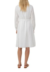 Vestito bianco realizzato in tessuto leggero, con maniche lunghe, vita con cintura e intricati motivi a occhiello in tutto il capo.
