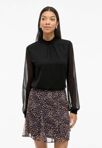 Maglietta nera a maniche lunghe con scollatura a volant e maniche trasparenti, abbinata a una gonna corta a strati con una stampa leopardata marrone e blu.