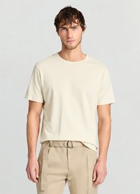 T-shirt beige à manches courtes en tissu texturé avec un col rond, associé à un pantalon crème avec passants de ceinture et une coupe slim.