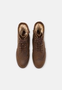 Botas de tobillo de cuero marrón con acabado texturizado, detalles de brogue y forro de piel sintética, con cierre de cordones y cremallera lateral.