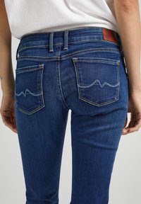 Jeans de mezclilla azul oscuro con un ajuste slim, que cuentan con dos bolsillos traseros y costuras curvas en el bolsillo derecho. Parche de cuero de la marca en la cintura.