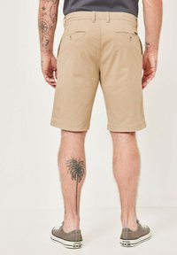 Beige cotton shorts with a straight cut, featuring two back pockets and a hemmed finish, worn with gray canvas shoes.