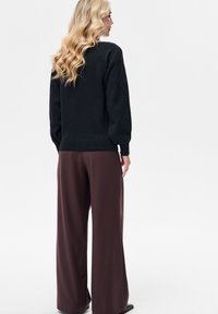 Czarny sweter dziany z bufiastymi rękawami w połączeniu z brązowymi spodniami o szerokich nogawkach. Wyraźna faktura swetra oraz gładka tkanina spodni.