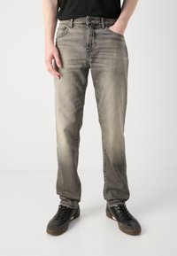 Jeans in denim grigio chiaro con finitura sbiadita, vestibilità regolare, gambe dritte, cinque tasche e dettagli neri sulle scarpe.